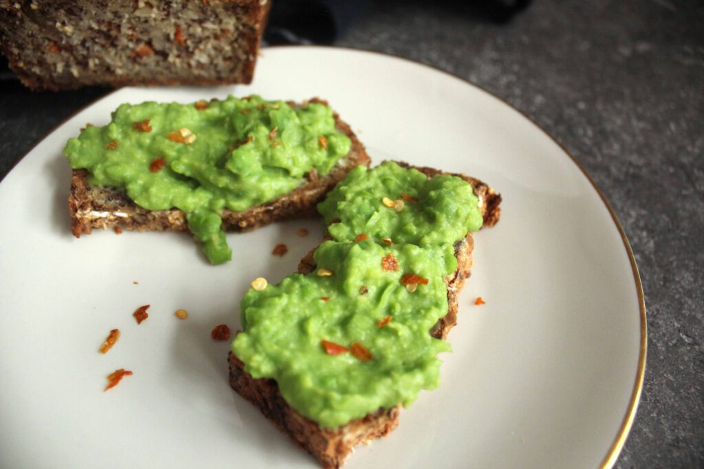 zwei Scheiben Brot mit Erbsenaufstrich auf Goldrandteller